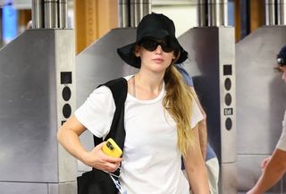 Jennifer Lawrence wearing a black hat, black sunglassses, a white t-shirt, and a black shoulder bag.