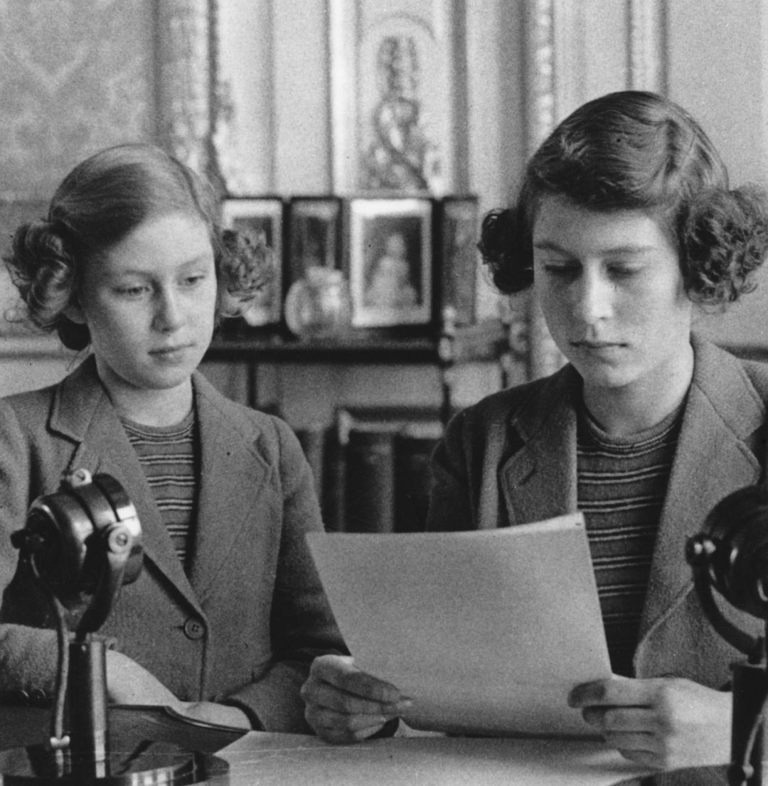 Princess Elizabeth and Princess Margaret reading off a paper at a desk