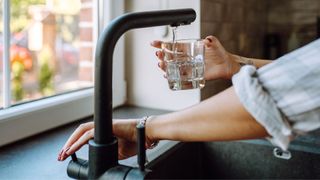 Woman putting glass under faucet of water