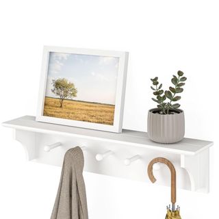 A white wall shelf with a framed print and plant on top, and a gray coat and umbrella being hung from it
