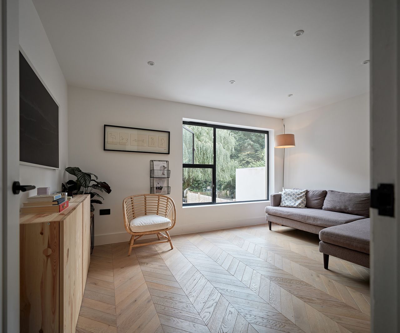 a sleek Scandi style living room in a self build house with a grey corner sofa and wicker armchair