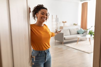 Woman opening door and gesturing welcoming viewer to come in