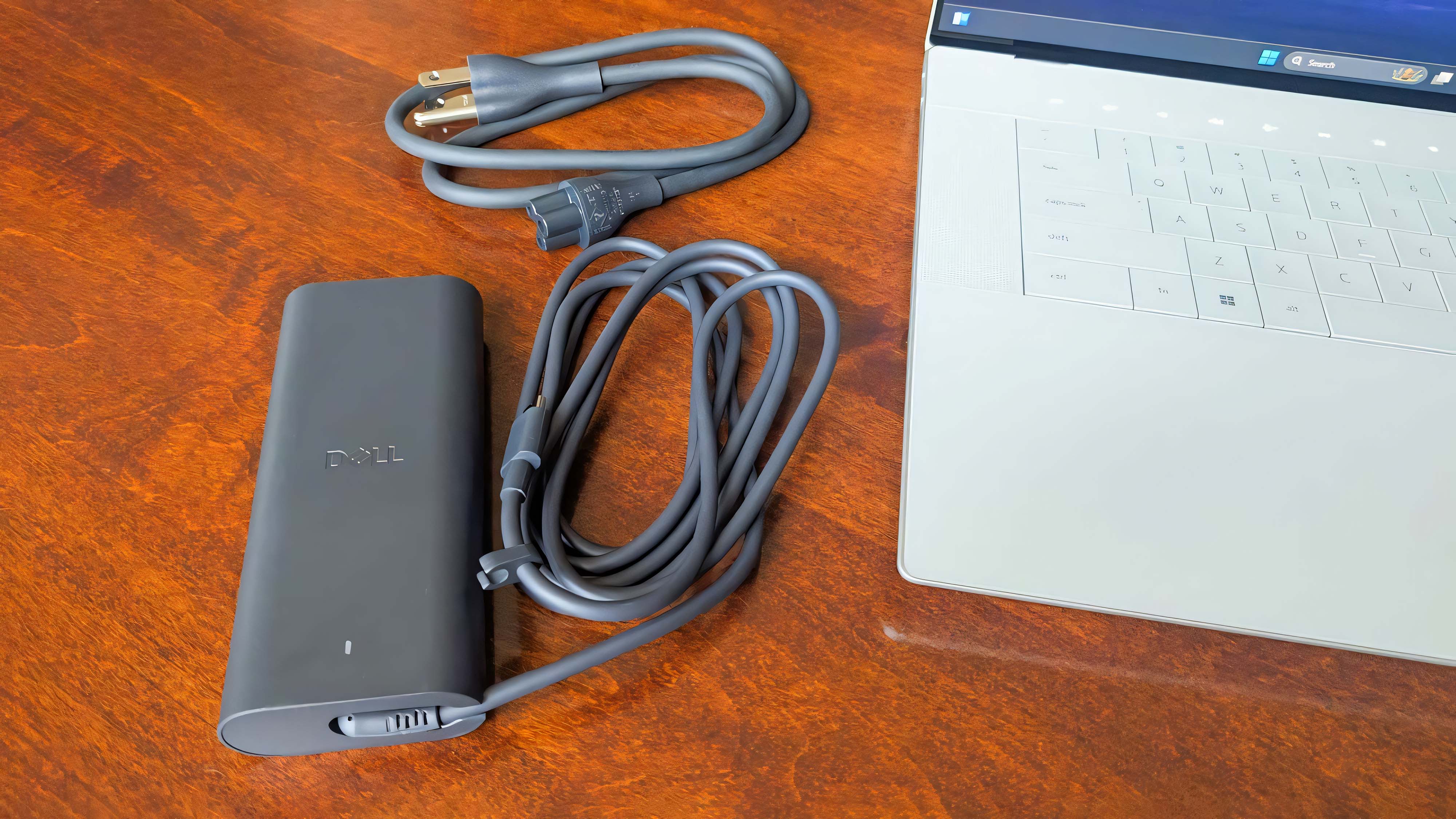 The Dell 16 Premium charging cable sitting next to the laptop.