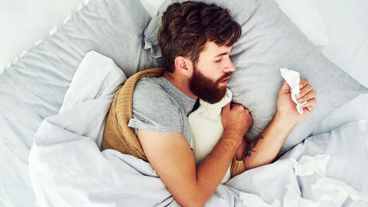 A dark haired man with hayfever tries to sleep with a runny nose