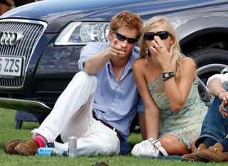 Prince Harry and Chelsy Davy sit by a car and point to photographers