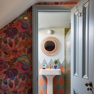 view into a bathroom with wallpaper on the main room wall and a tiled splashback in the bathroom