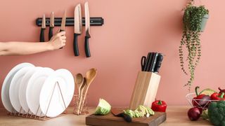 Someone taking a knife from a magnetic knife strip next to plates and a knife block with knives