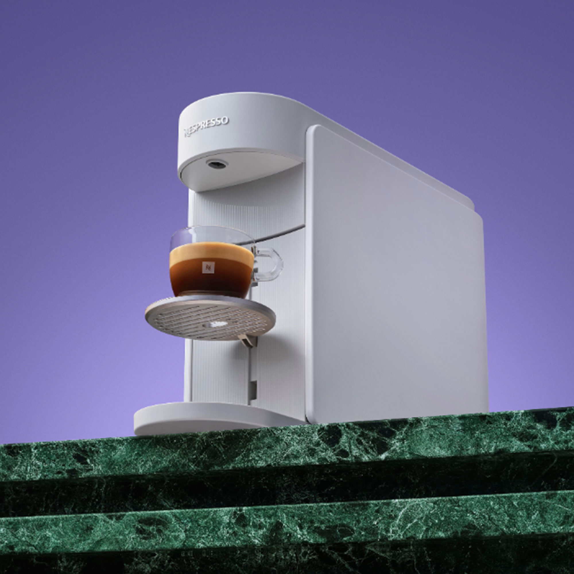 White Nespresso Vertuo Up coffee machine on green marble worktop in front of purple background