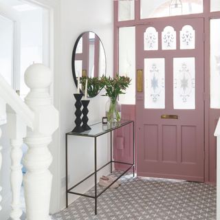 White painted hallway with patterned tiled floor leading to a pink front door