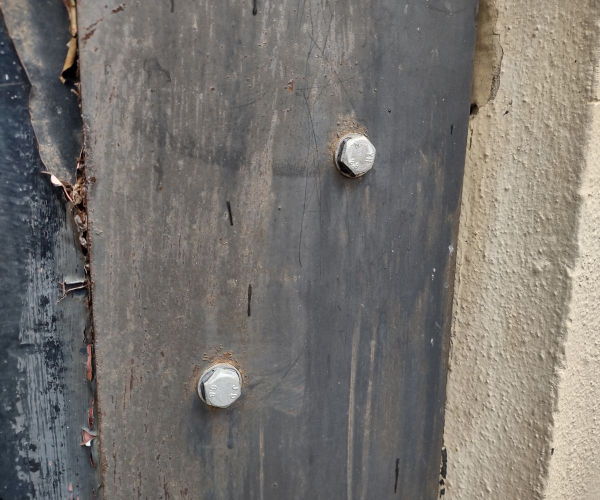 Two heavy duty screw bolts fastened into a grey exterior wood wall