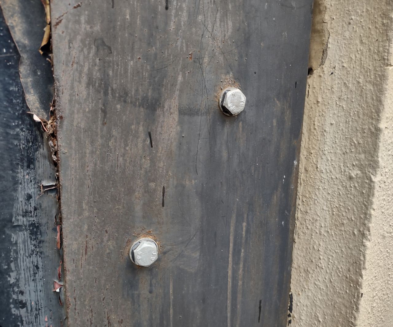 Two heavy duty screw bolts fastened into a grey exterior wood wall
