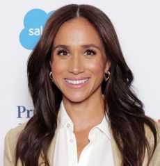 Meghan Markle wearing a tan suit standing in front of a white background