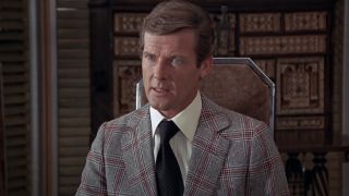 Roger Moore sits in conversation with a stern expression in The Man With The Golden Gun.