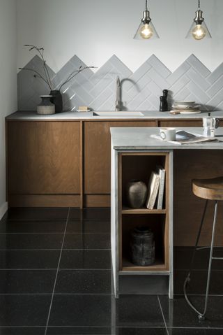 Black granite floor tiles in kitchen with herringbone white and grey wall tiles, marble topped kitchen island and wooden seat bar stools