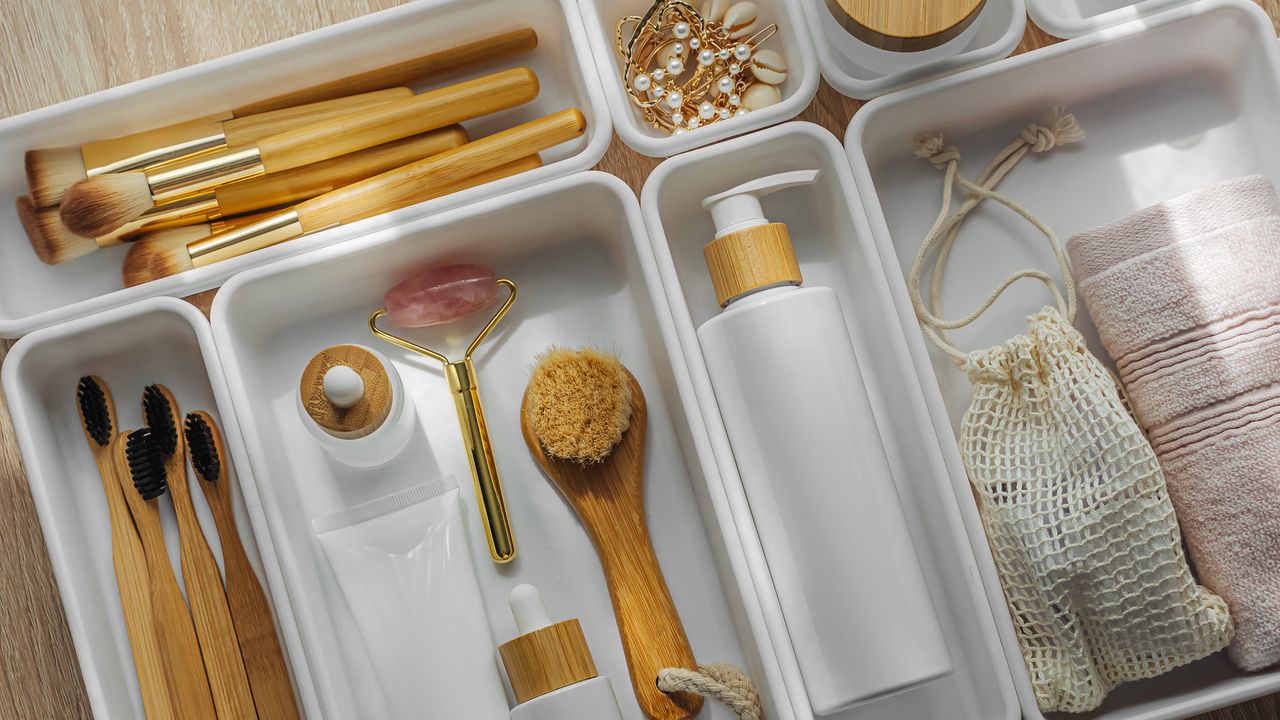 An image of a drawer with white drawer dividers filled with beauty and self-care products including bamboo makeup brushes and rose quartz face roller