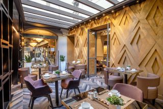 In a hotel, tables are ready for guests to enjoy breakfast in a room with wooden walls and flooring.