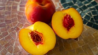 two peaches, one is cut in half, on mosaic counter top