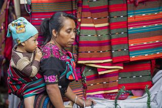 A Mayan woman with a baby on her back sells colorful fabrics at the Chichicastenango market in Guatemala