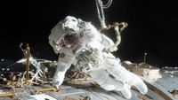 A spacesuited astronaut floats outside of a space station.