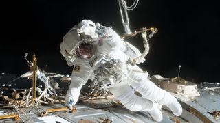 A spacesuited astronaut floats outside of a space station.