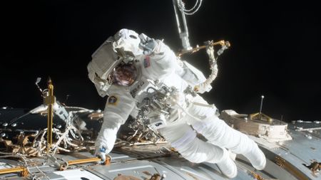 A spacesuited astronaut floats outside of a space station.
