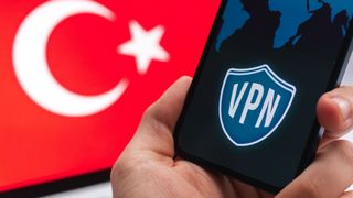 Homme avec un smartphone à la main avec le logo VPN à l'écran et le drapeau turc en arrière-plan.
