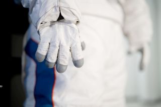 another closeup of a white spacesuit glove, with the rest of the white suit in the background.
