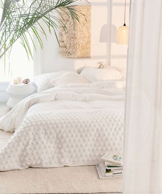 A white bedroom with mattress on floor and pendant light with palm tree houseplant decor