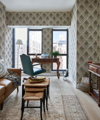 office with patterned wallpaper and rug, blue chair, leather sofa and wooden desk