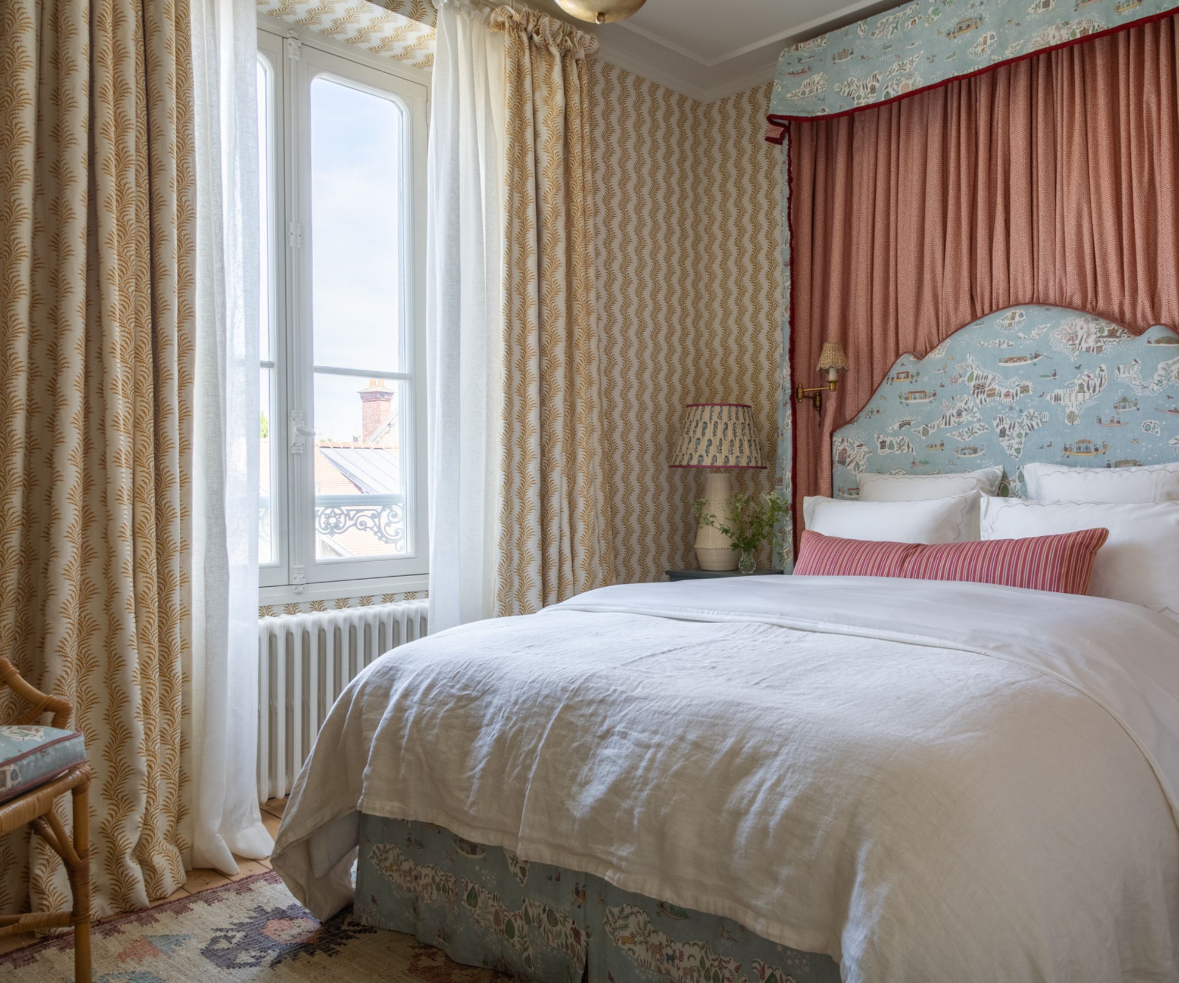 large hotel style bedroom with neutral and soft warm yellow striped wallpaper and matching curtains, an upholstered pale blue patterned canopy bed and headboard