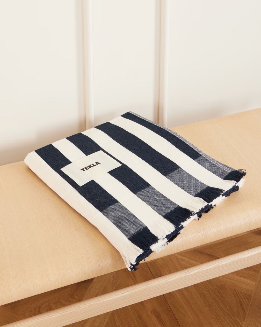 Folded striped towel in black and white fabric, resting on a pale wood bench.