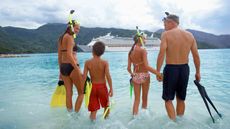 Parents with children (10-12) in water with snorkel gear, rear view, cruise ship in background
