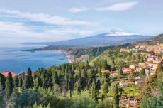 The hilltop town of Taormina overlooking Giardini Naxos bay, facing snow-capped Mount Etna.