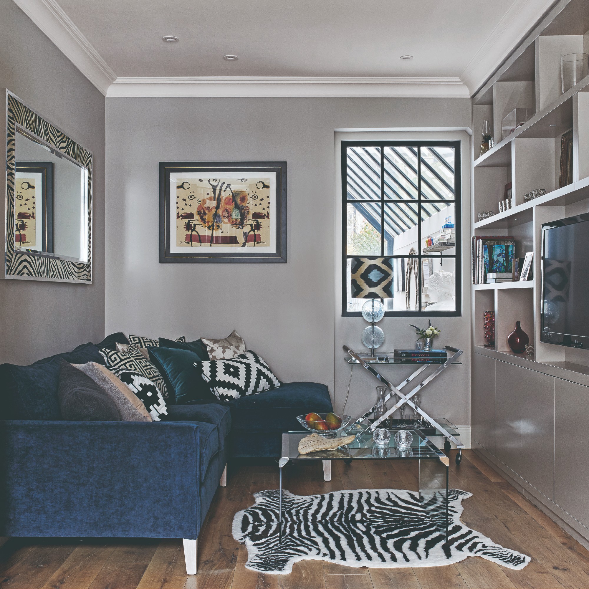 A grey living room with a chaise dark blue sofa, patterned cushions and a faux tiger skin rug