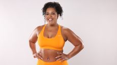 Woman in yellow sports bra and leggings standing with her hands on her hips smiling at camera