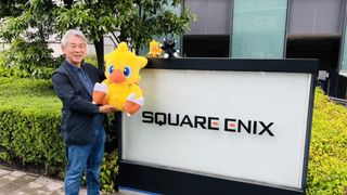 Shinji Hashimoto holds up a chocobo plush in front of a Square Enix sign.