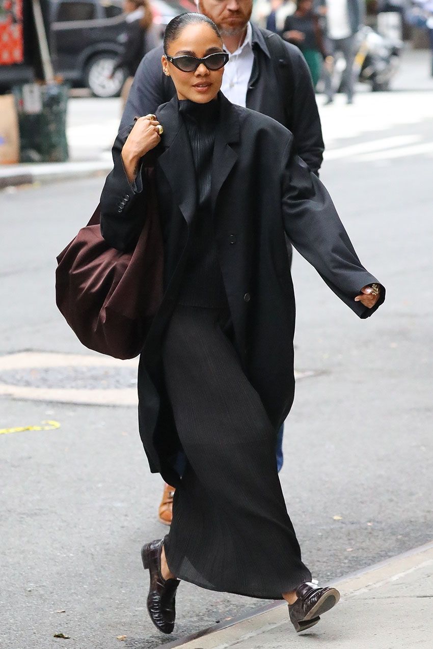 Tessa Thompson wearing a black coat, a plisse top and skirt, brown loafers