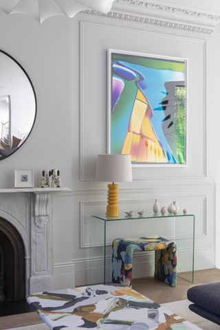 A small pale gray living room with colorful statement art and lamp above an acrylic table.
