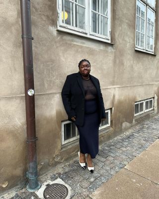 Woman wears black sheer shirt, black maxi skirt, and black oversize blazer while posing on Copenhagen street.