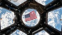 an american flag against a round glass window through which earth can be seen from space