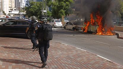 IDF soldiers walk past a burning car in Israel