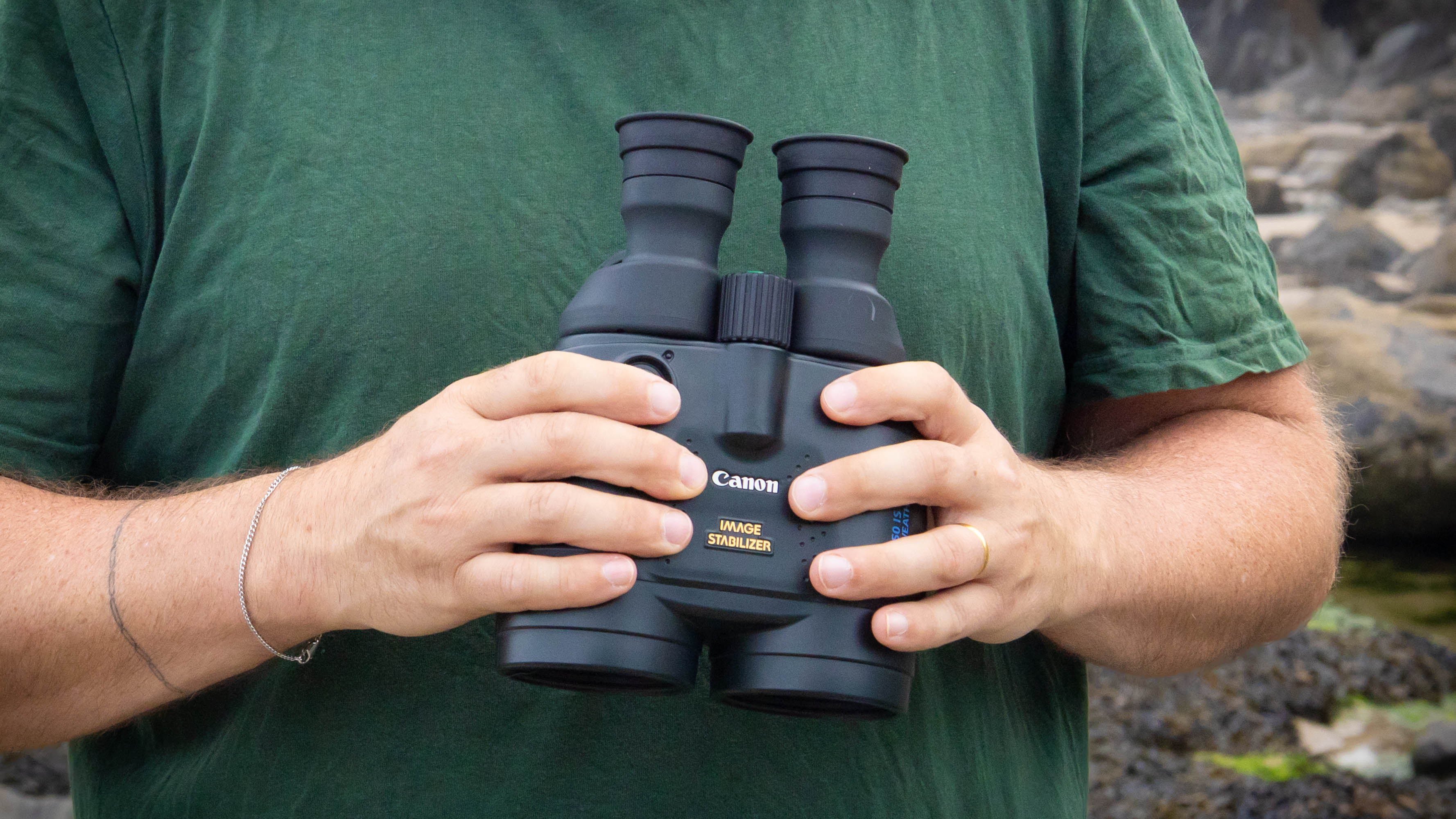 A male holding the Canon 15x50 IS binoculars, showing the Canon logo.