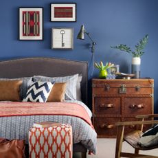 Blue bedroom with upholstered headboard, gallery wall and patterned footstool