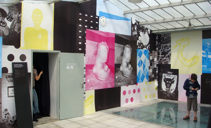 Linus Bild exhibition. A room with paintings all over the walls, white floor tiles and a skylight.