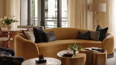 living room with mustard yellow sofa, nesting coffee tables, armchair, beige sheer curtains, floor lamp, and dining table behind