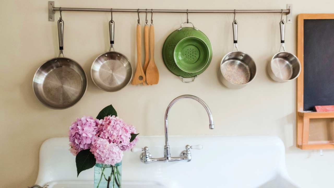 Multiple stainless steel pots and pans hanging above a farmhouse kitchen sink