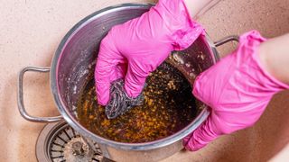 Person scrubbing burnt pot with pink rubber gloves