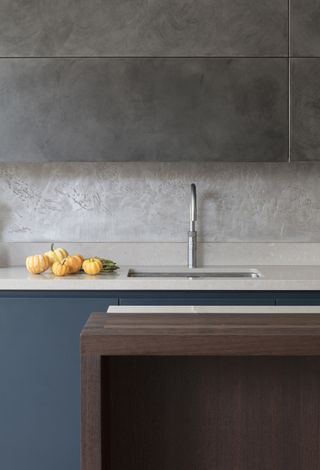 Concrete effect cabinets, polished plaster backsplash, white marble countertops in a modern handlelesskitchen