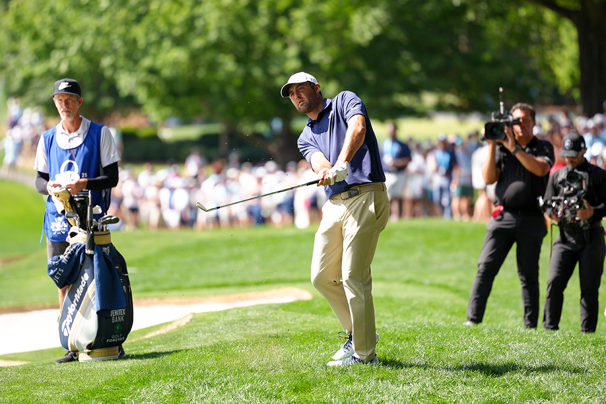 Scottie Scheffler in the finish position after hitting a shot in front of a television camera at Quail Hollow for the PGA Championship