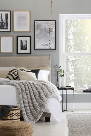 Grey and white bedroom with gallery wall by Furniture Choice, knitted gray blanket, white floorboards, gray rug, black metal side table, baskets, upholstered bed, black and white bed pillows